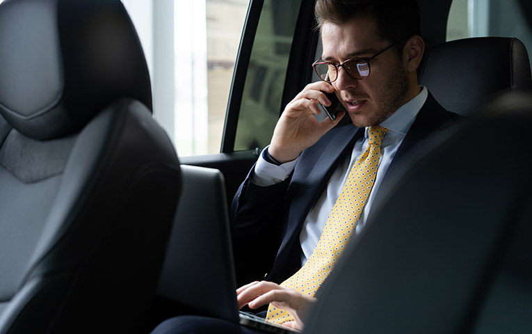 Businessman working on laptop and phone in the back seat of a Tokyo luxury chauffeur car