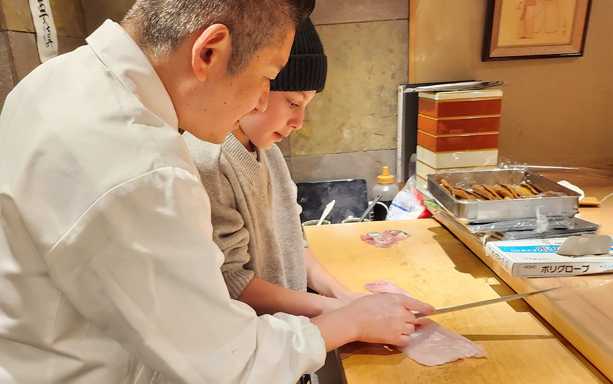 A chef providing hands-on assistance with fish cutting techniques