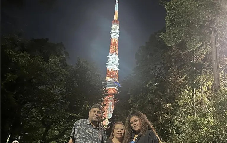 夜の東京タワーを背景に、記念撮影をする3人の男女。